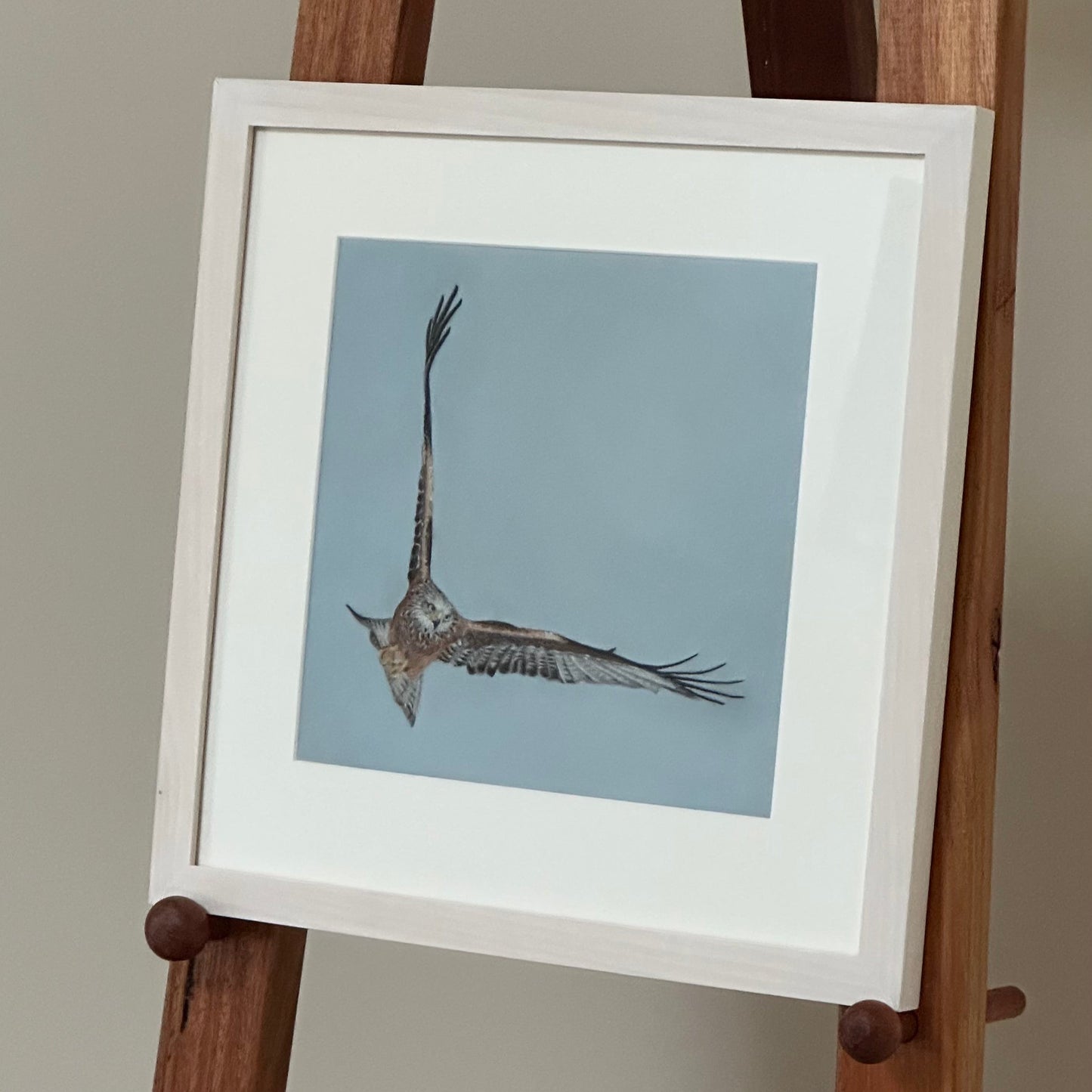 Framed artwork of a bird in flight on a wooden easel against a plain background