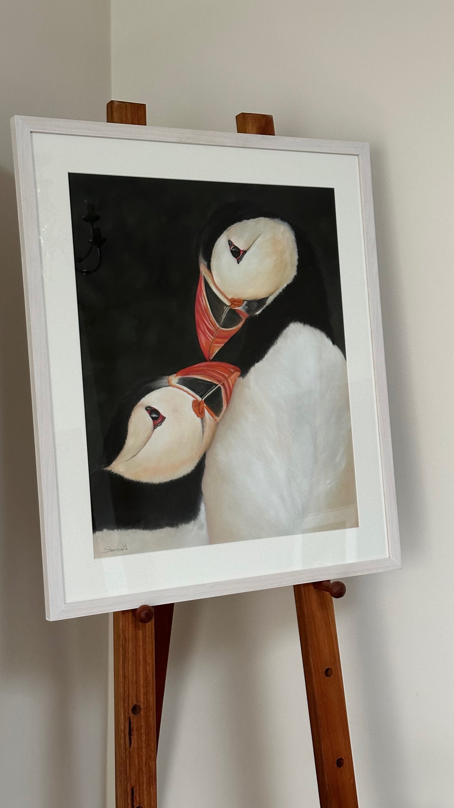 Framed artwork of a puffin on an easel against a white wall