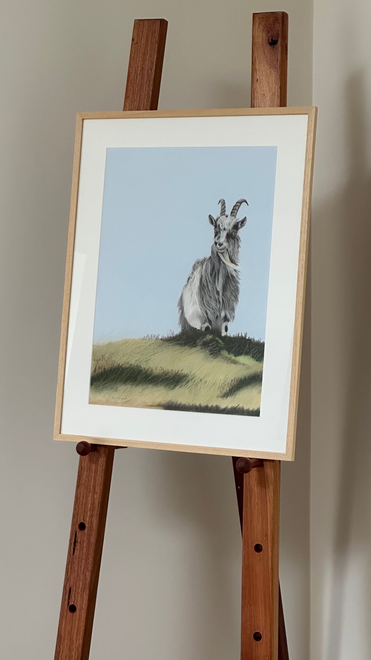 Framed painting of a goat on a wooden easel against a plain wall
