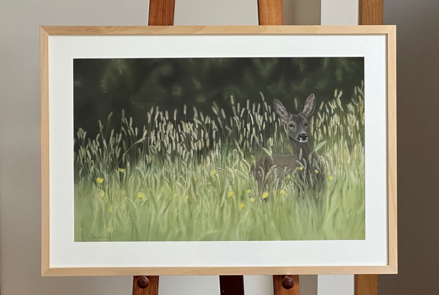 Framed artwork of a deer in a grassy field on an easel.