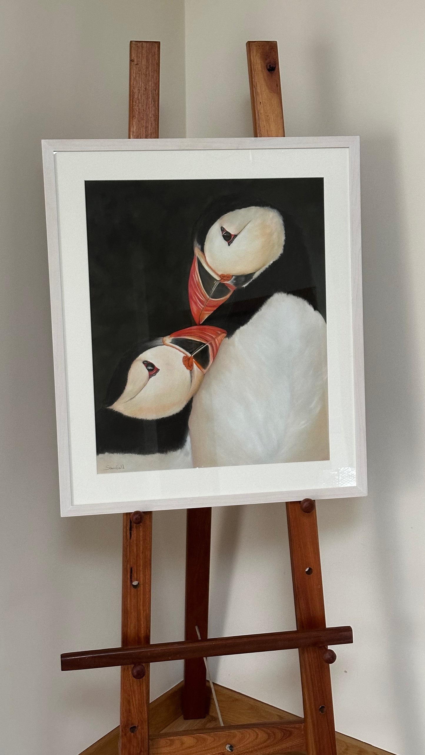 Framed artwork of a puffin on a wooden easel against a plain wall.