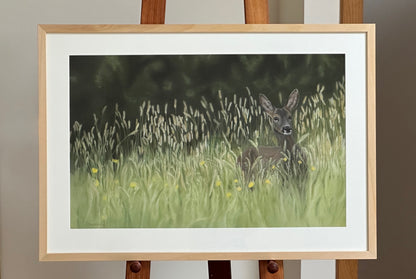 Framed artwork of a deer in a grassy field on an easel.
