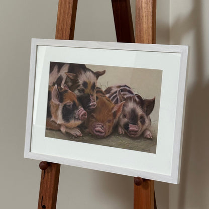 Framed photograph of pigs on a wooden easel against a plain wall.